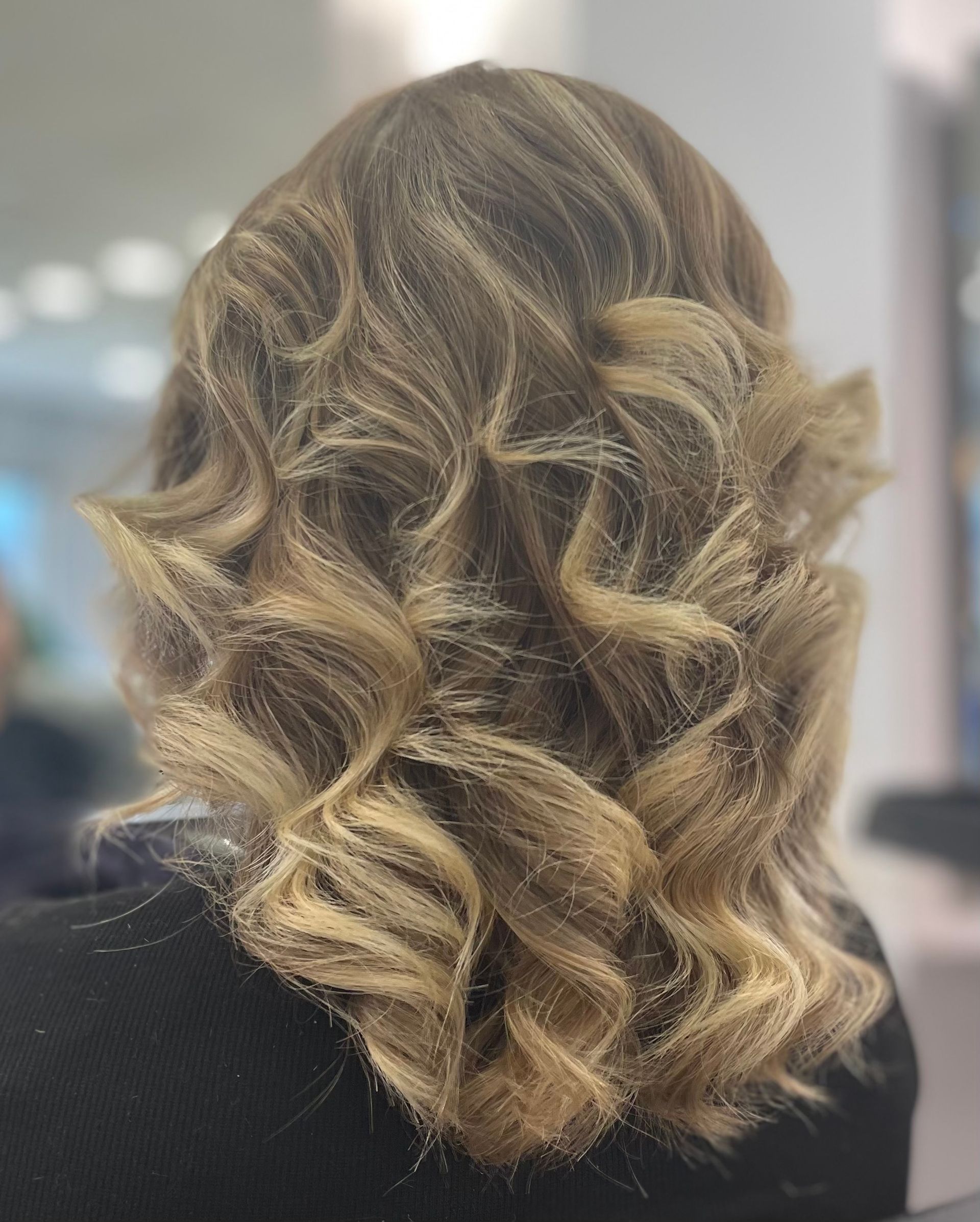 Une femme de dos avec les cheveux blonds et bouclés