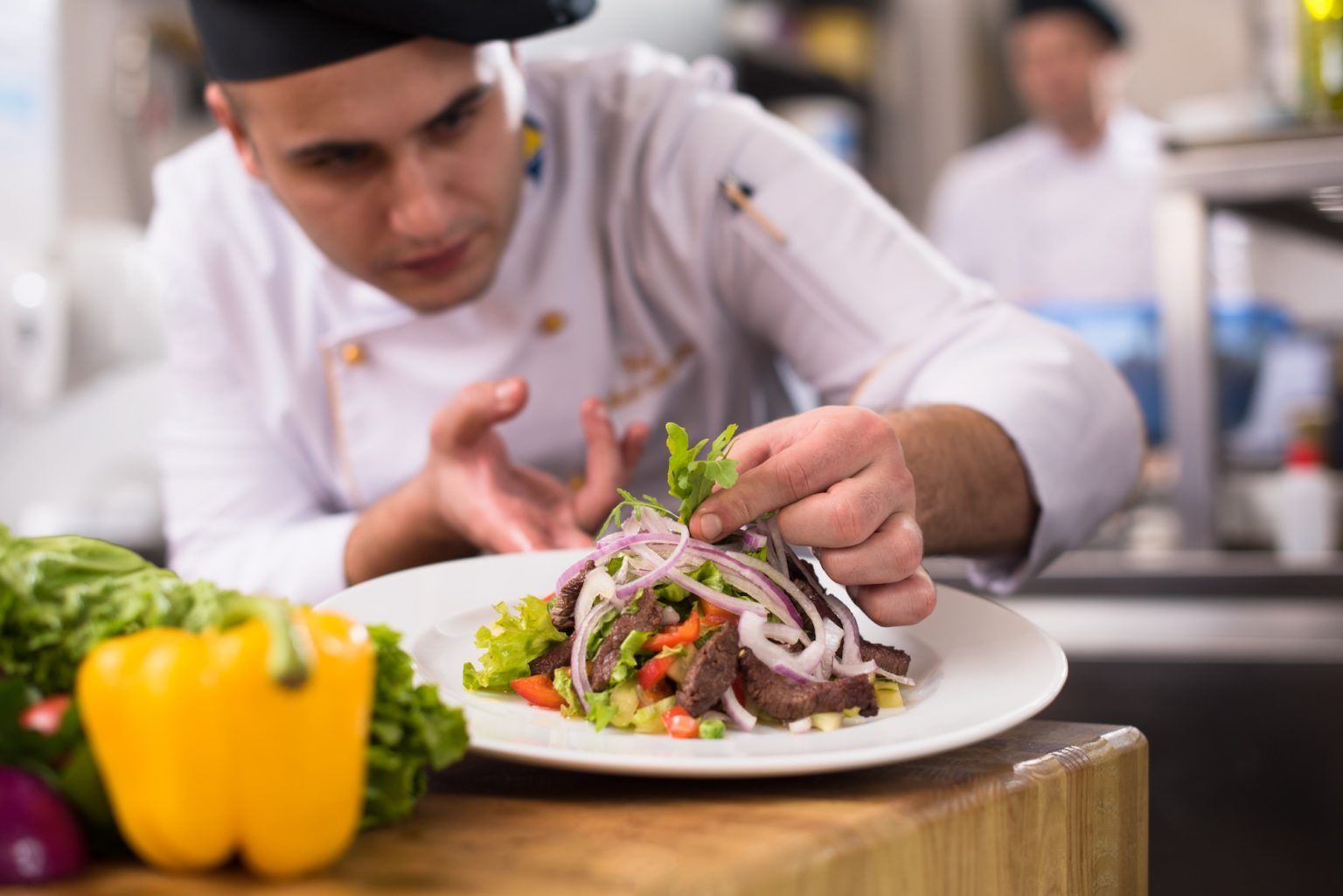 Un chef prépare une salade dans une assiette dans une cuisine.