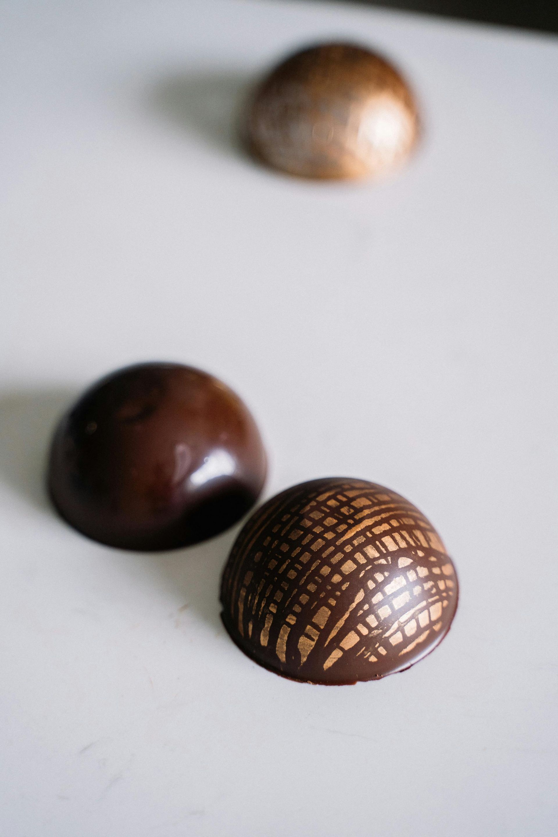 Trois dômes en chocolat, deux devant, un avec des lignes dorées.