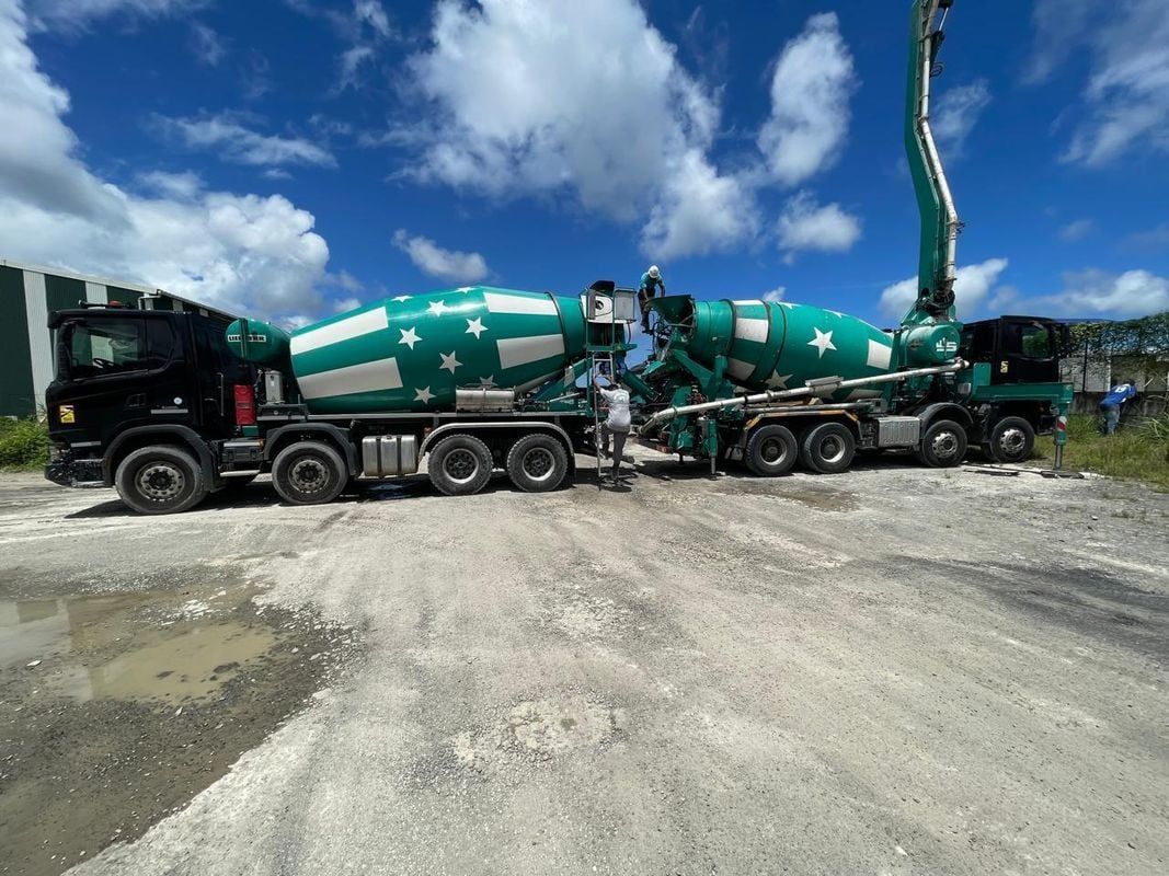 Deux camions-toupies verts à motifs d'étoiles sur un chantier. L'un des camions a sa pompe déployée.