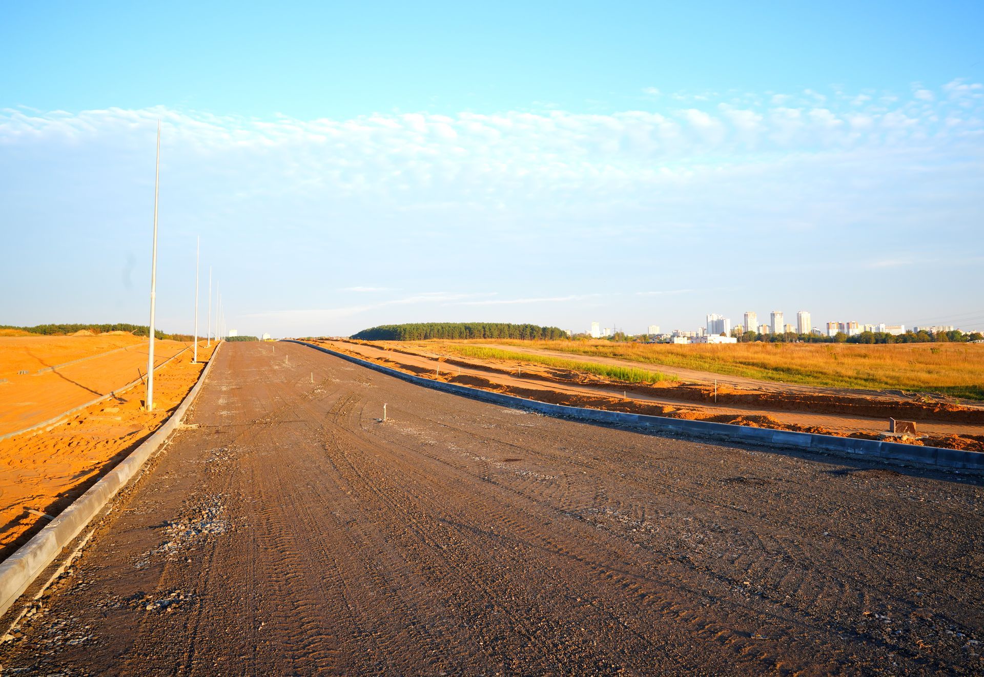 Une route asphaltée traverse un chantier de construction et se dessine sur la silhouette de la ville sous un ciel bleu.
