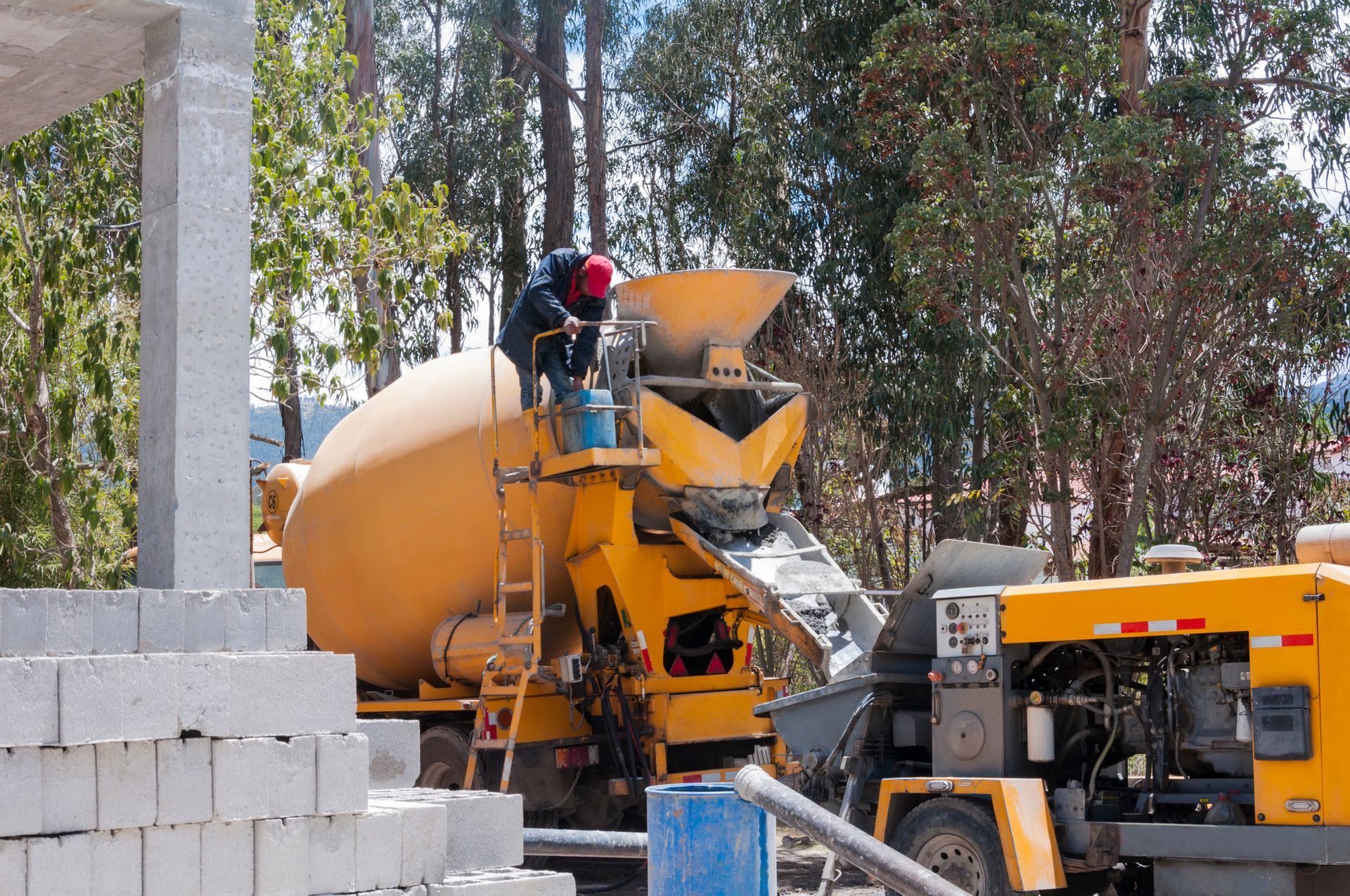 Un homme conduit un malaxeur à béton jaune sur un chantier de construction, en train de couler du béton.