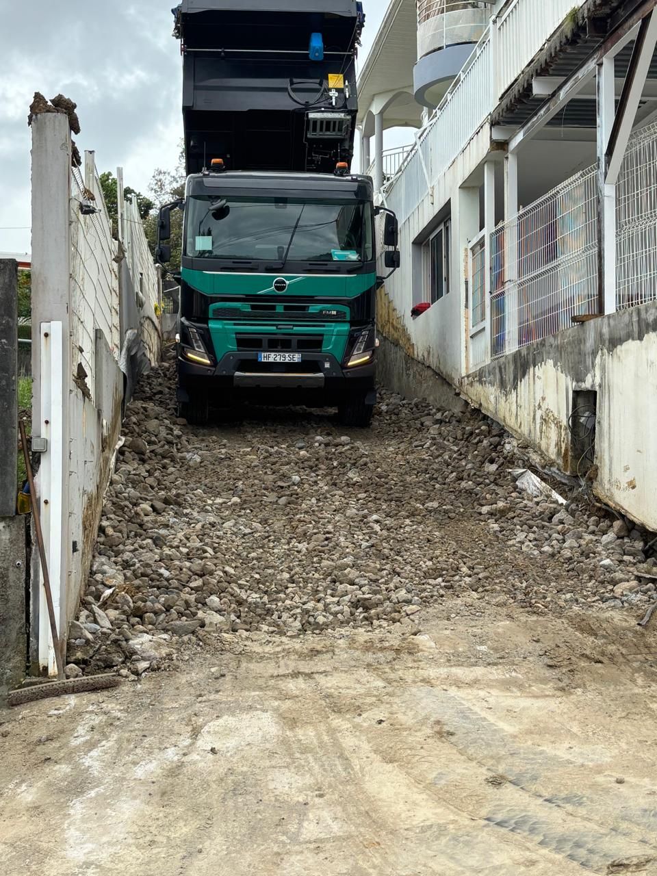 Une personne utilise une règle à niveler pour égaliser du ciment frais sur un chantier. Des piquets jaunes marquent les niveaux.