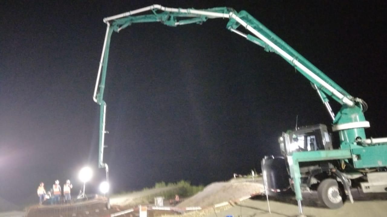 Du béton est déversé sur une surface à l'aide d'un tuyau bleu, créant une masse grise et humide.