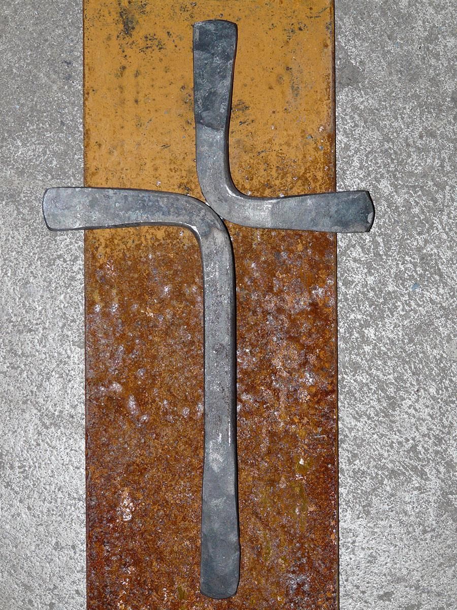 Ein Metallkreuz sitzt auf einem rostigen Stück Metall
