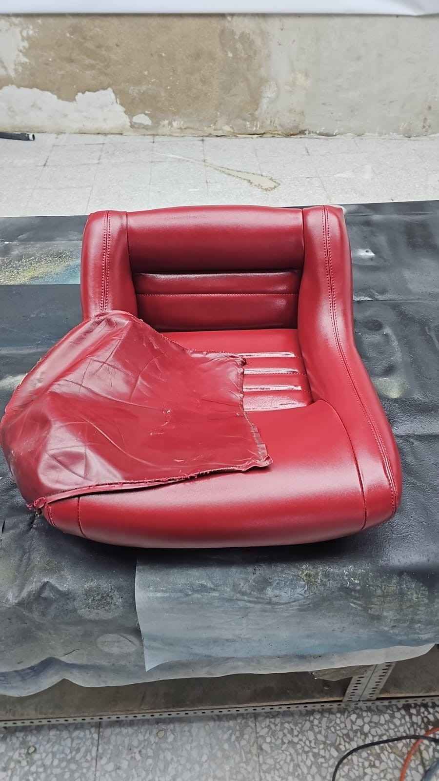Cojín de silla de vinilo rojo rasgado sobre una mesa oscura contra una pared desgastada.