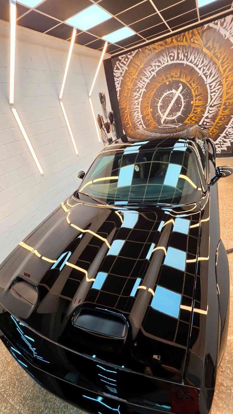 Un coche deportivo negro en una sala de exposición con luces blancas brillantes y una vitrina.