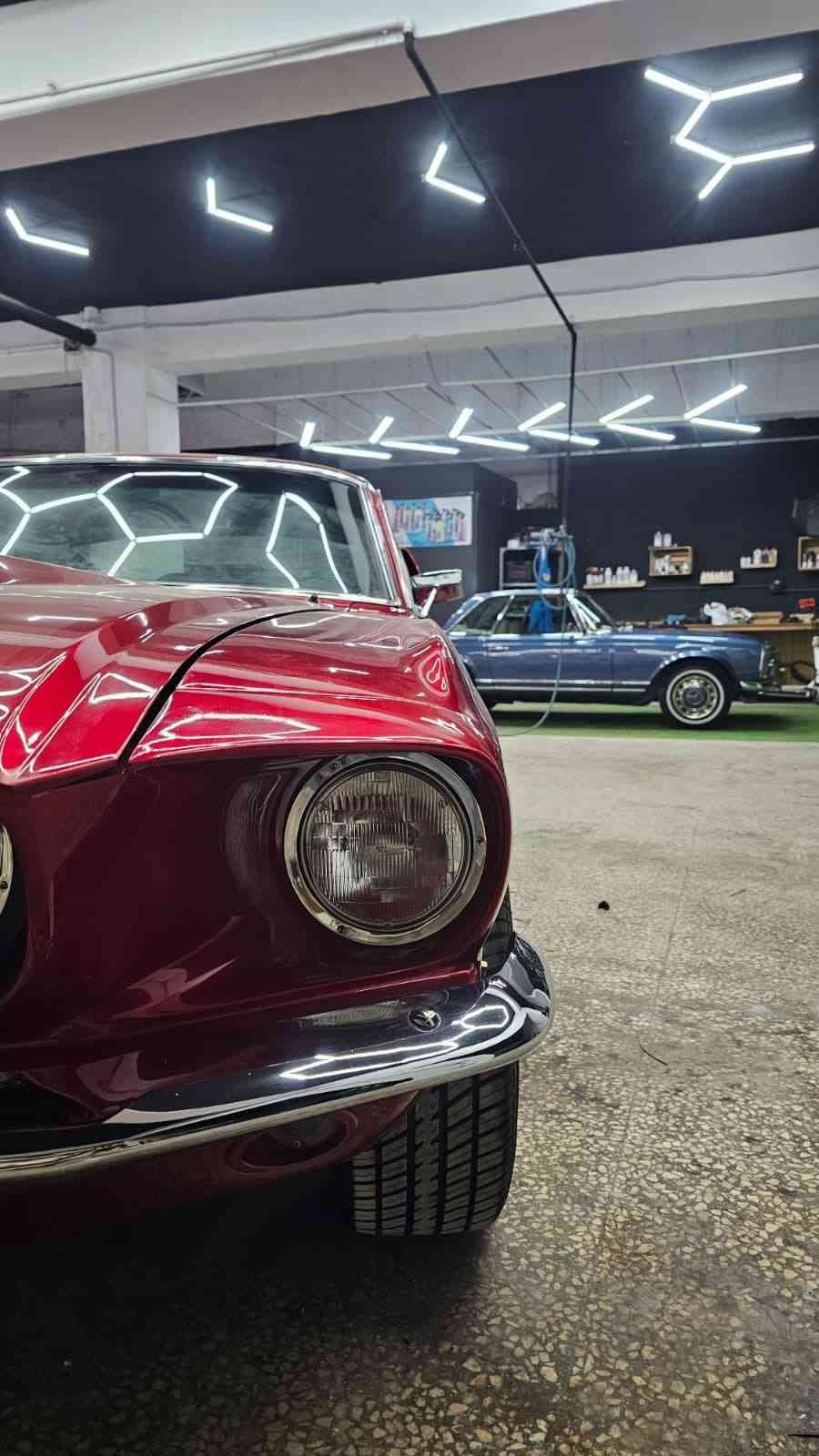 Primer plano de un coche antiguo rojo por la noche en un garaje, con un coche clásico azul al fondo.
