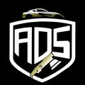 Logotipo del escudo de ADS con un coche dorado y una cuchilla sobre fondo negro