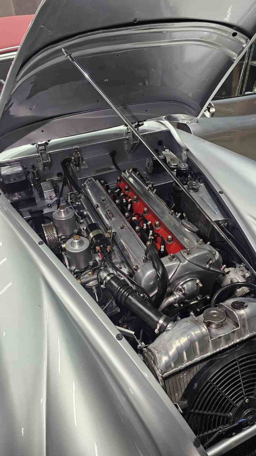 Primer plano del compartimento del motor de un coche deportivo plateado con el capó abierto.
