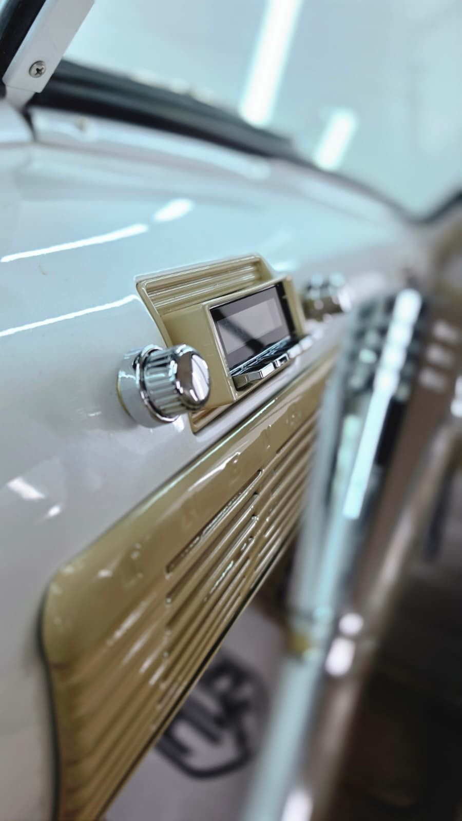Primer plano del salpicadero color beige y el mando cromado de la radio de un coche clásico.