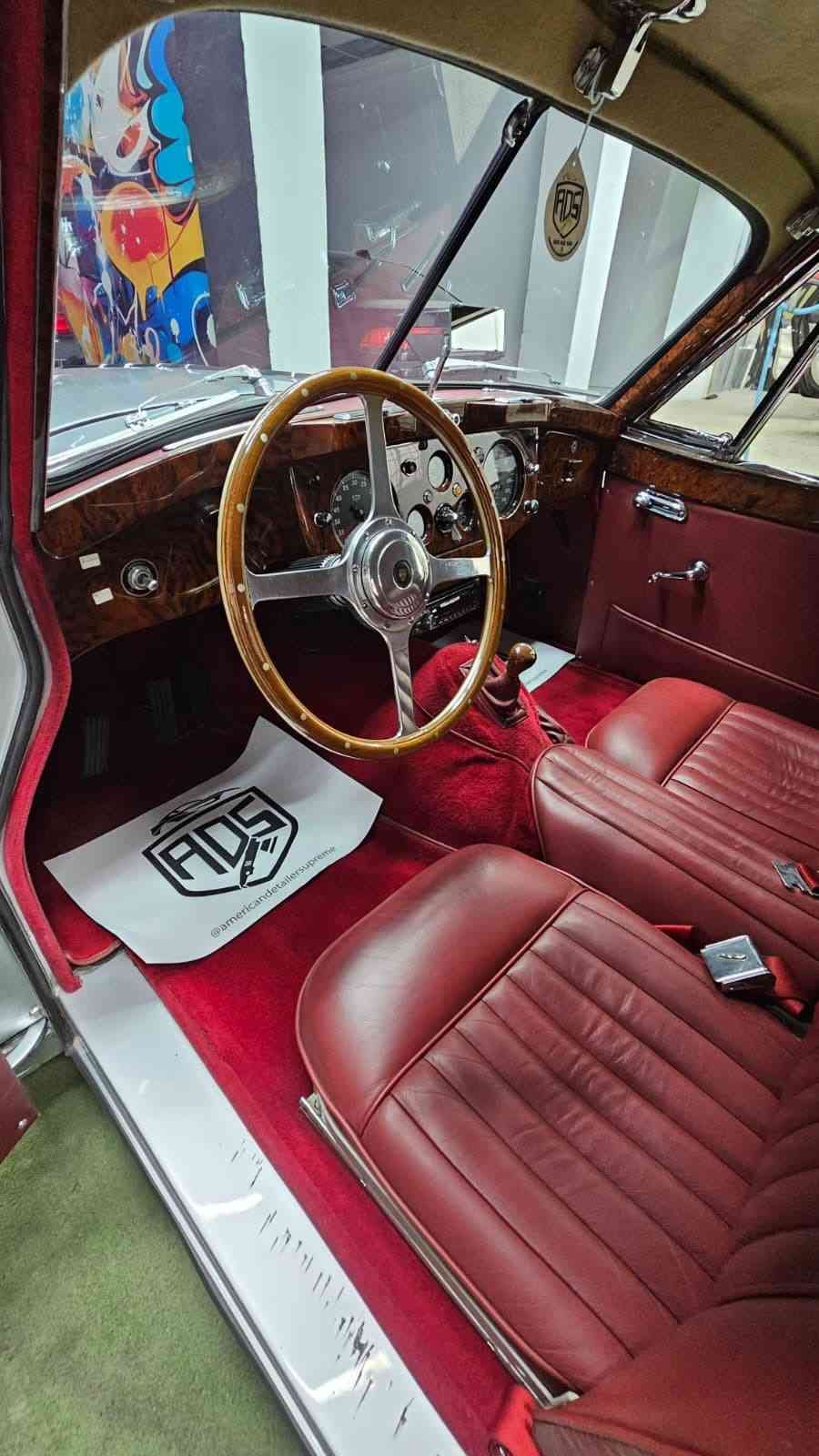 Interior de coche clásico con asientos de cuero rojo, volante de madera y salpicadero pulido.