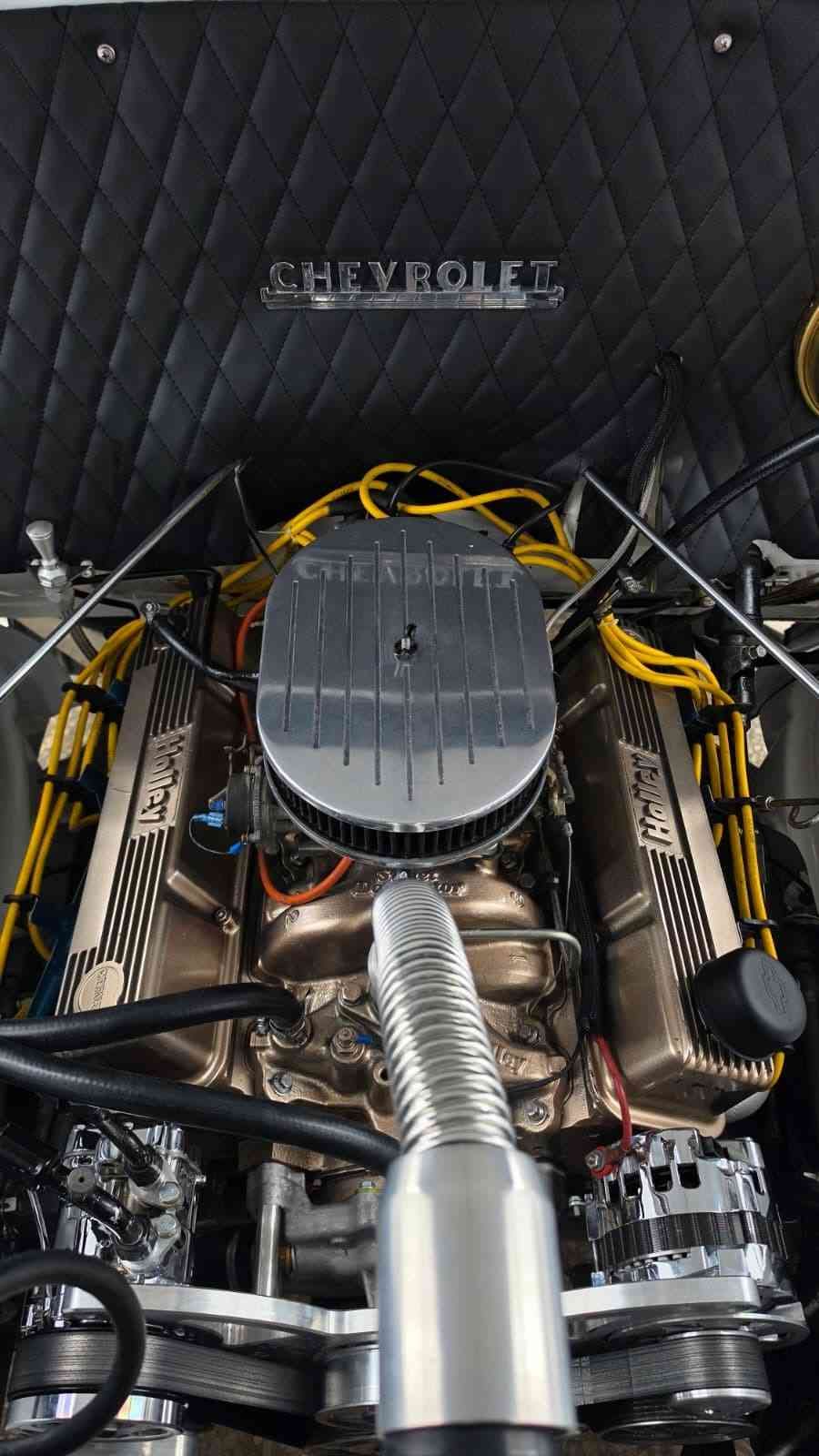 Compartimento del motor Chevrolet con filtro de aire cromado, cableado amarillo y revestimiento del capó negro acolchado.