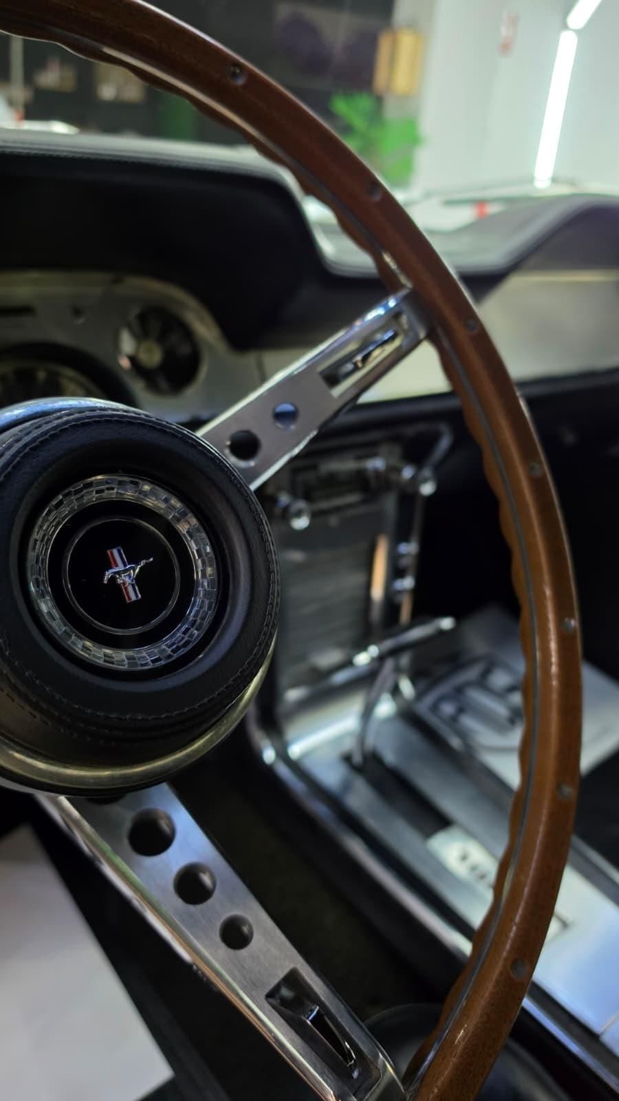 Volante y salpicadero de madera del interior de un coche clásico, con la palanca de cambios manual a la vista.