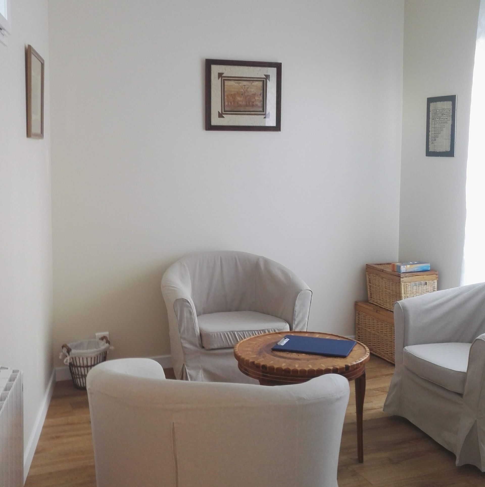 Coin salon confortable avec chaises blanches, petite table et tableaux encadrés aux murs.