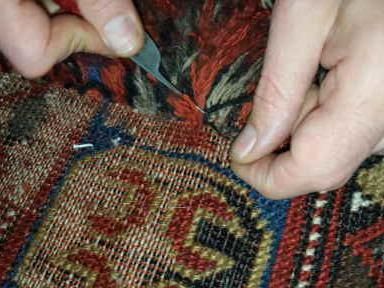 Eine Person schneidet mit einer Schere ein Loch in einen Teppich.