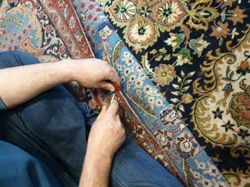 Eine Person schneidet mit einer Schere einen Teppich zu.