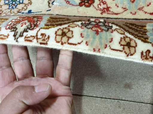 Eine Person hält ein Stück Teppich mit den Fingern.