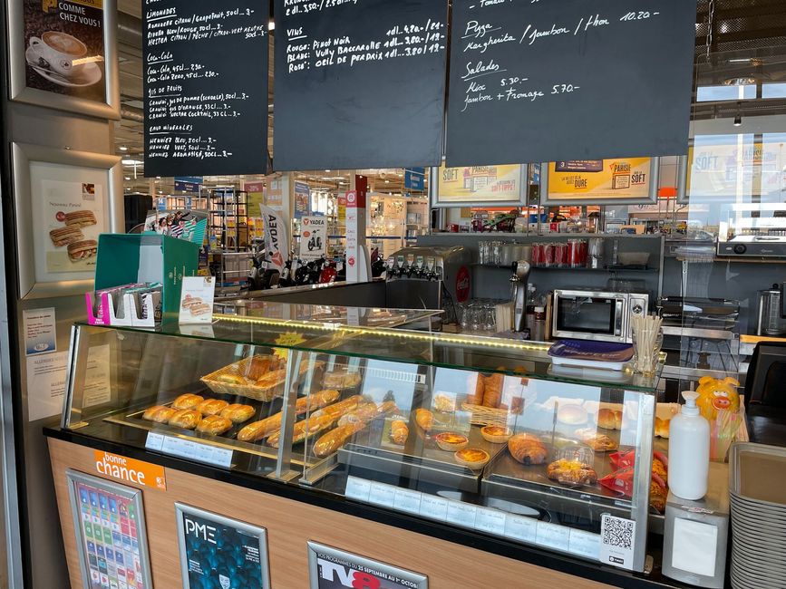 Comptoir de boulangerie avec pâtisseries en vitrine et menus affichés au-dessus d'une vitrine de café