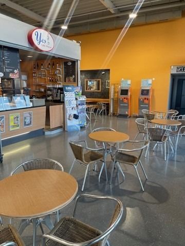 Coin salon lumineux d'un café avec des tables rondes, des chaises en métal et un mur jaune-orange derrière le comptoir.