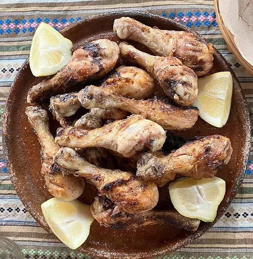 Un plato de muslos de pollo a la parrilla con rodajas de limón sobre una mesa.