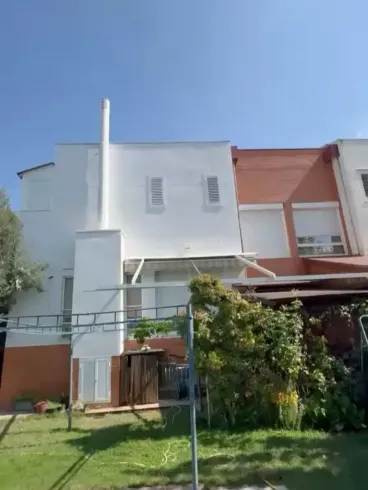 Edificio residencial de dos plantas, con paredes blancas y naranjas, un balcón y un jardín delantero verde bajo un cielo azul