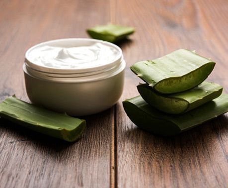 Hojas de aloe vera y un tarro de crema sobre una mesa de madera.