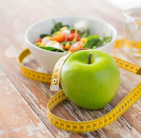 Una manzana verde con una cinta métrica alrededor junto a un tazón de ensalada.