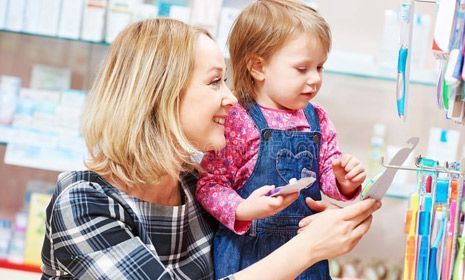 Una mujer y una niña miran cepillos de dientes en una farmacia.