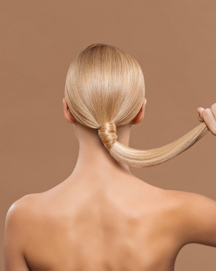 La espalda de una mujer con cabello rubio recogido en una cola de caballo.