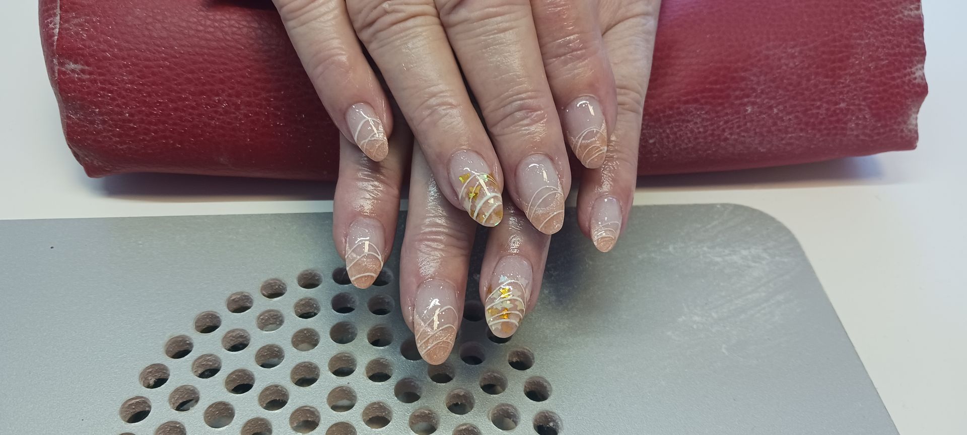 Die Nägel einer Frau liegen auf einem roten Kissen neben einem Nagellackentferner.