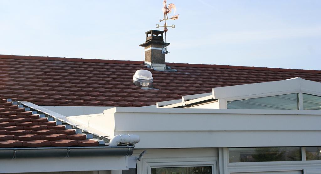 Maison avec une façade blanche, des tuiles rouges et une girouette sur le toit