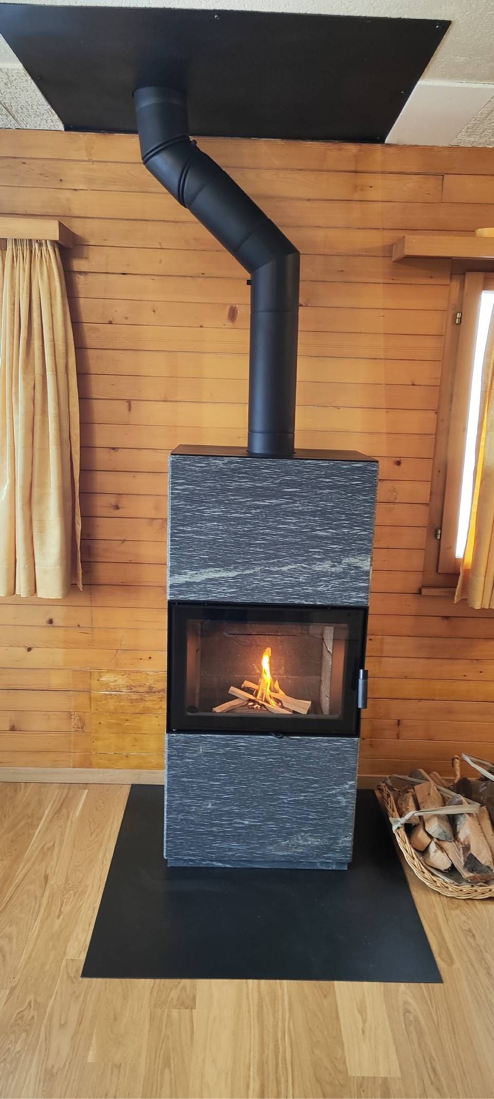 Schwarzer Holzofen mit brennendem Feuer im Inneren einer Holzhütte