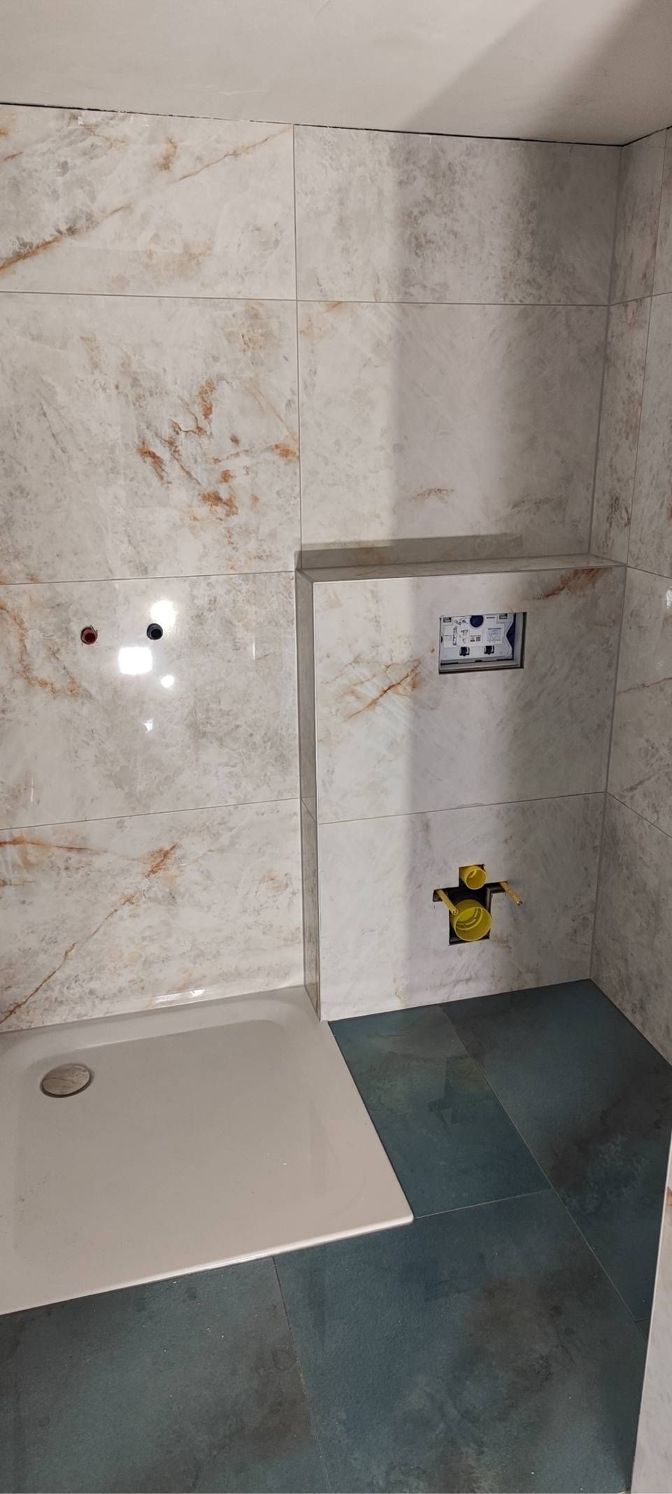 Kleines gefliestes Badezimmer mit wandmontiertem Waschbecken, blauer Fussmatte und Wänden in weiss-grauer Marmoroptik.