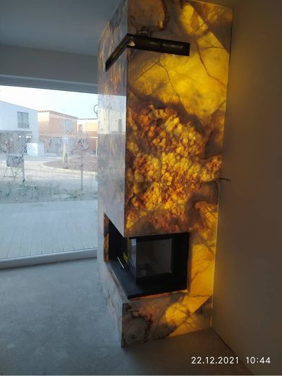 Ein Kamin mit bernsteinfarbenen Flammen brennt in einem modernen Zimmer neben einem grossen Fenster.