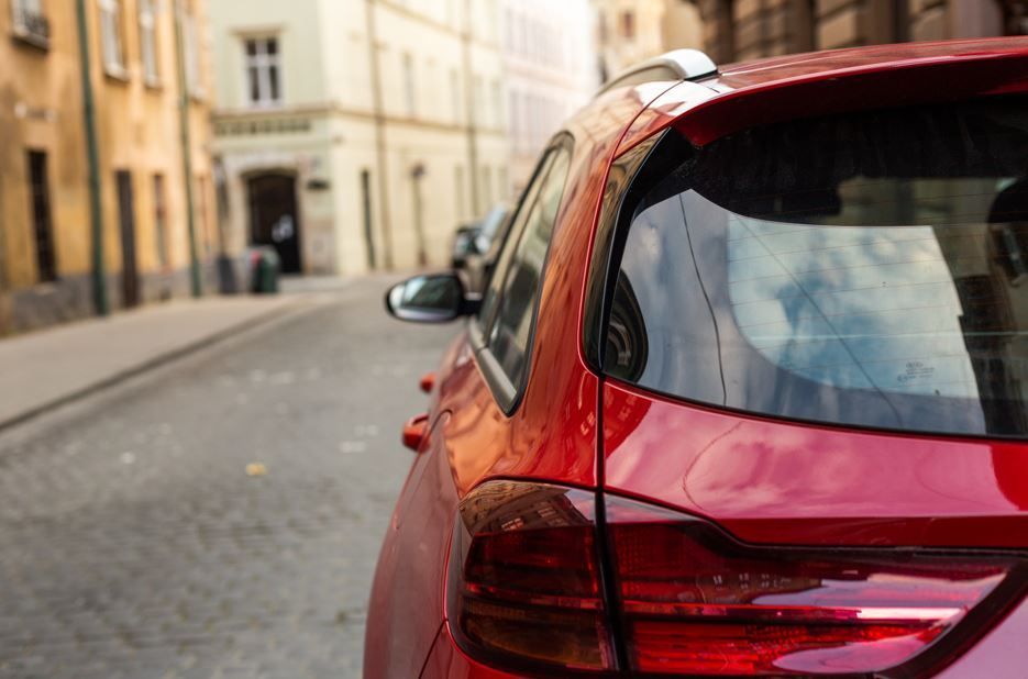 Coche rojo aparcado en una calle adoquinada de una ciudad europea, con edificios al fondo.