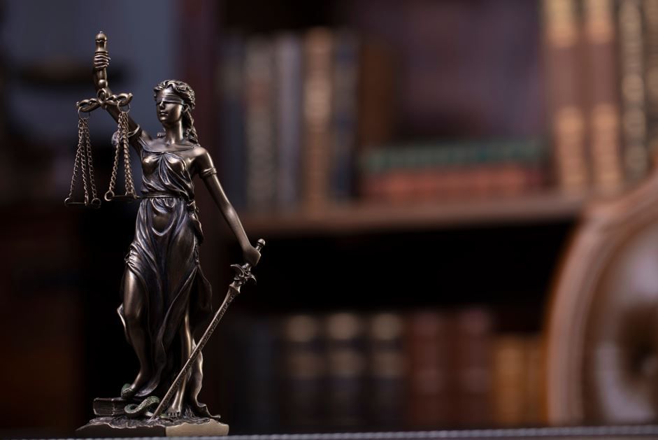 Estatua de la Dama de la Justicia sosteniendo una balanza y una espada, con estanterías al fondo.