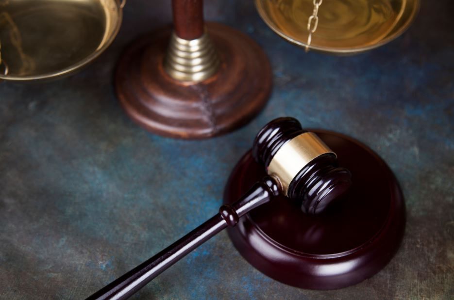 Martillo sobre un bloque de madera junto a una balanza; objetos asociados con la ley y la justicia.