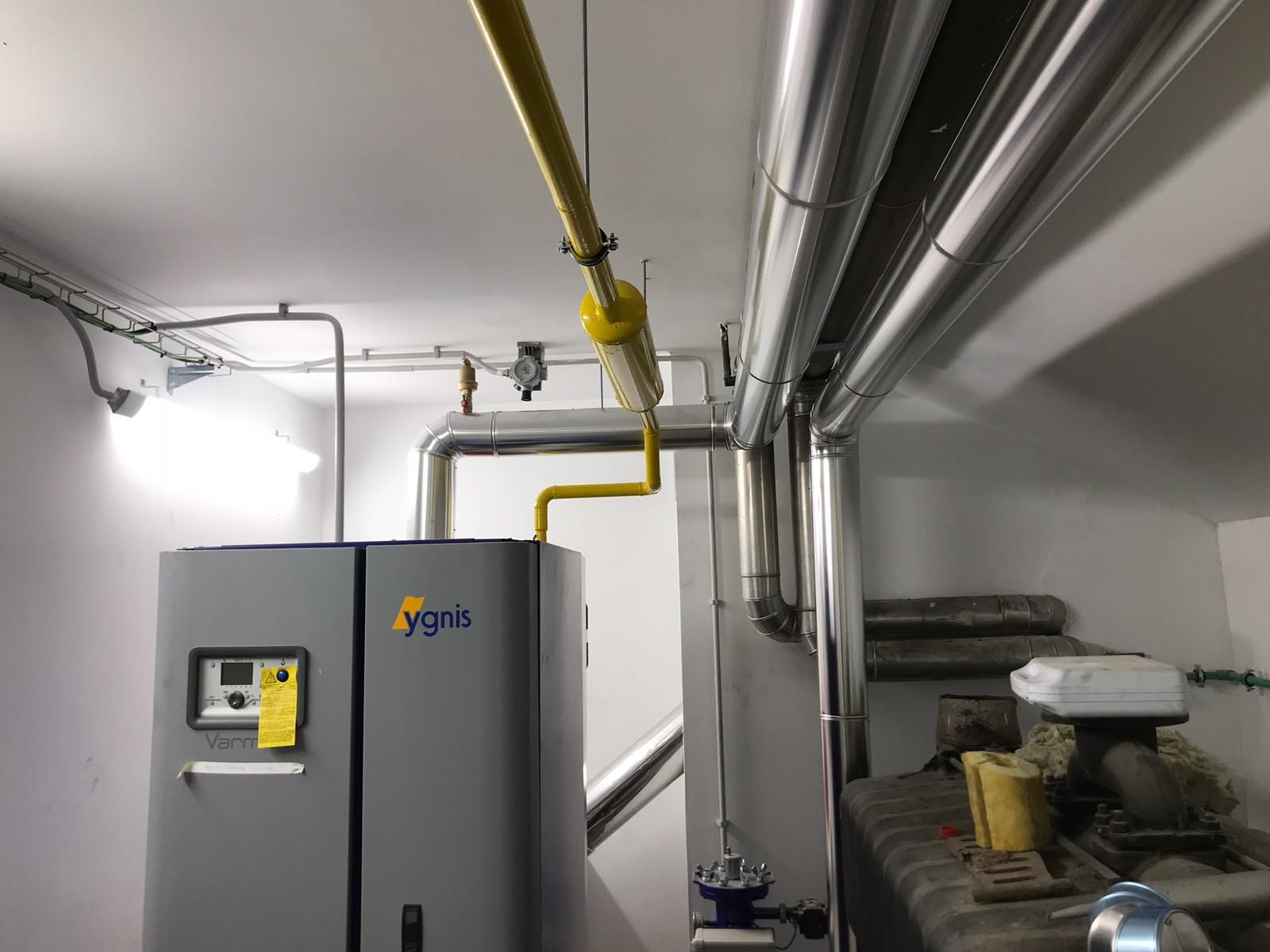 Una habitación con una caldera y tuberías colgando del techo.