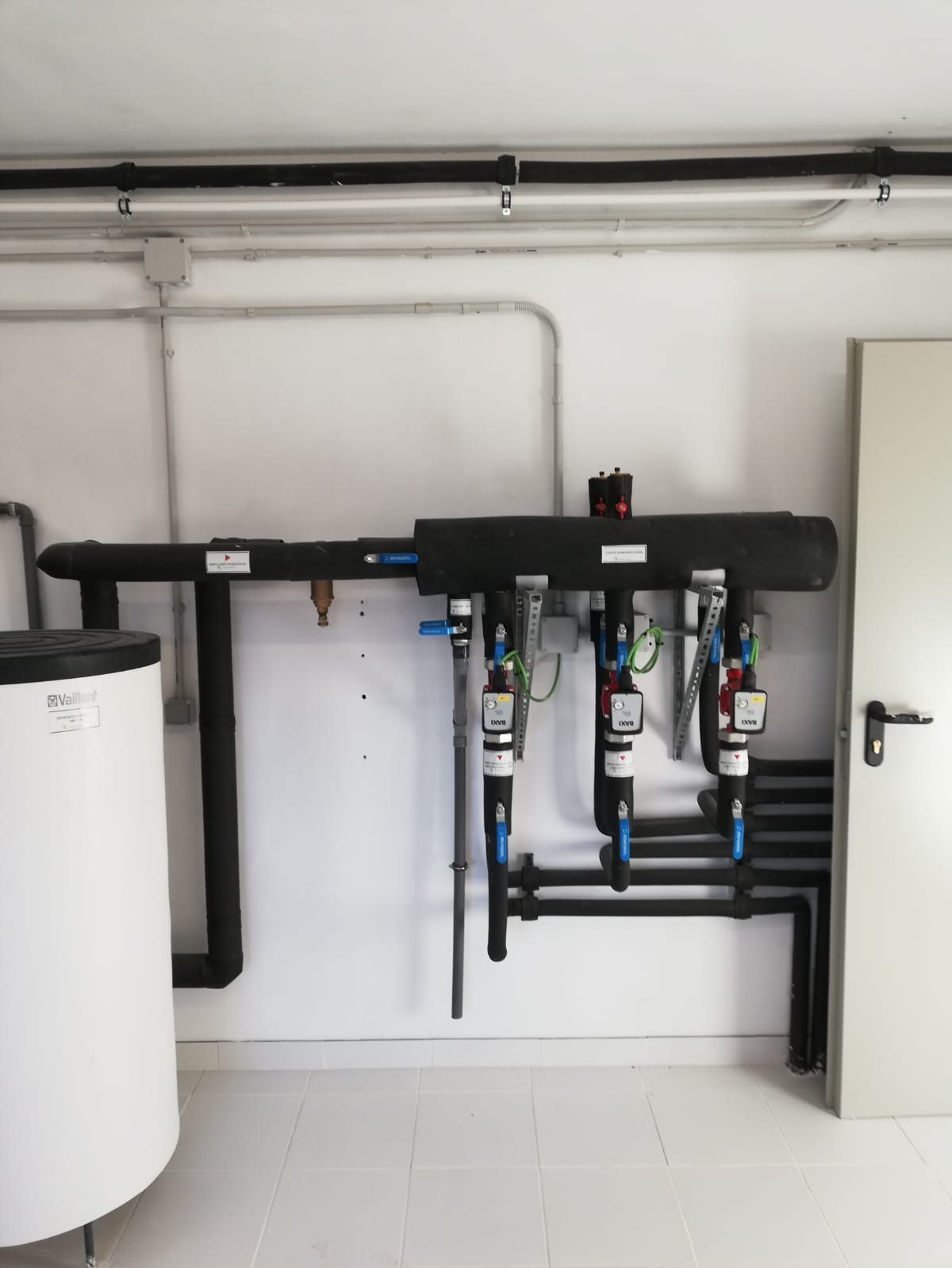 Una habitación con muchas tuberías y una puerta blanca.