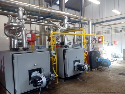 Dos calderas están ubicadas una al lado de la otra en una habitación con tuberías.