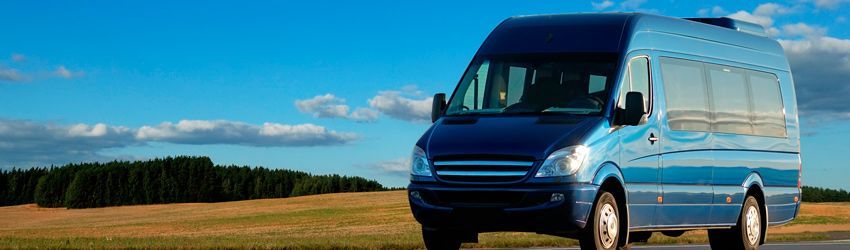 Una camioneta azul circula por una carretera al lado de un campo.