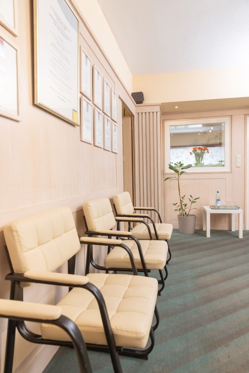Wartezimmer mit beigen Stühlen, Auszeichnungen an der Wand und grünem Teppich.