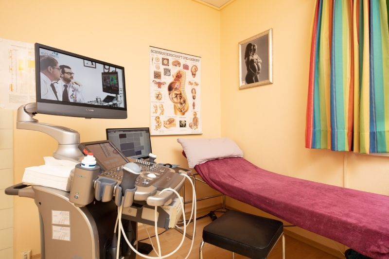 Ein Untersuchungsraum mit Ultraschallgerät, einer Krankenliege und anatomischen Tafeln an der Wand.