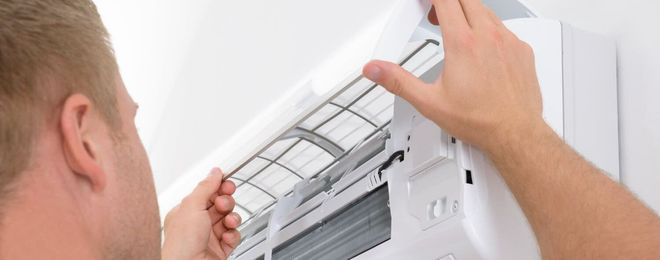 Un hombre está arreglando un aire acondicionado en una pared.