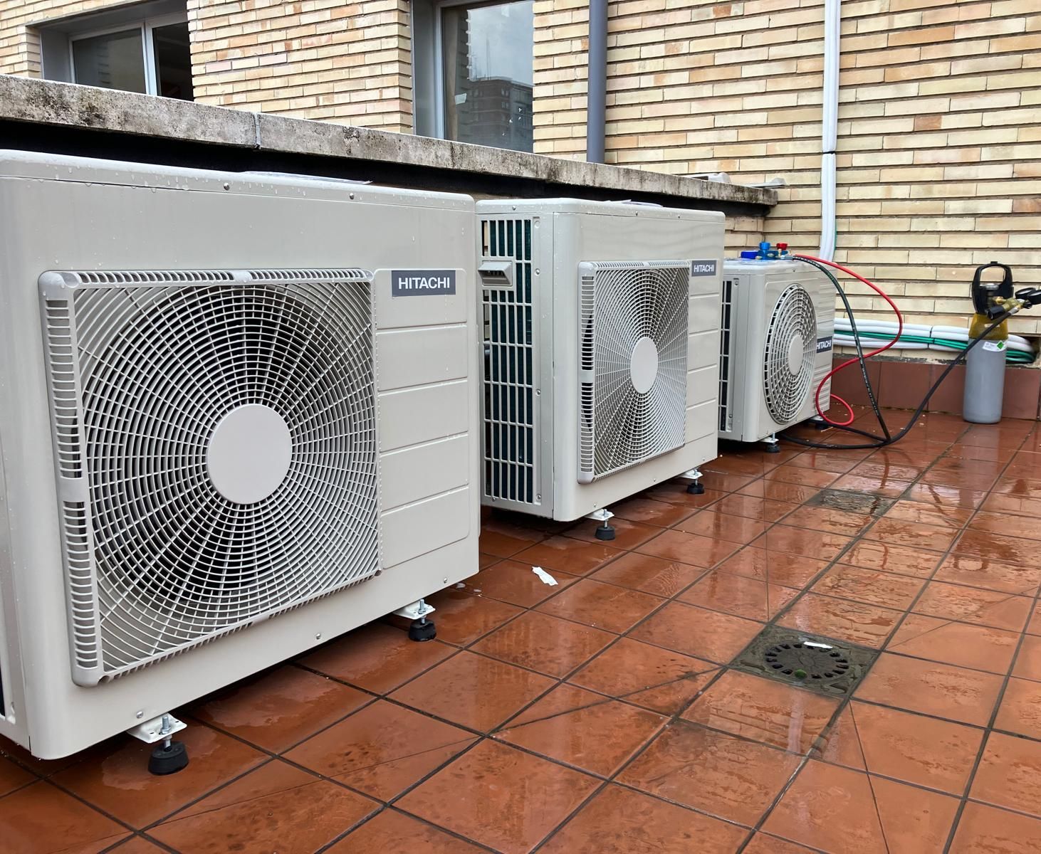 Tres aparatos de aire acondicionado están colocados sobre un suelo de baldosas delante de un edificio de ladrillos.