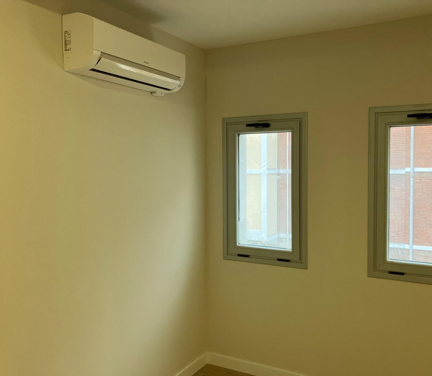 Una habitación con dos ventanas y un aire acondicionado en la pared.