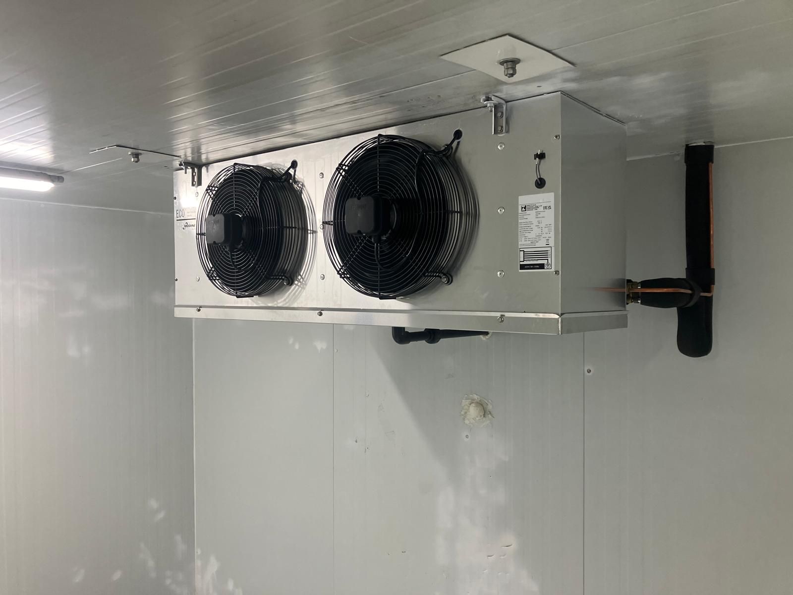 Un refrigerador con dos ventiladores colgando del techo.