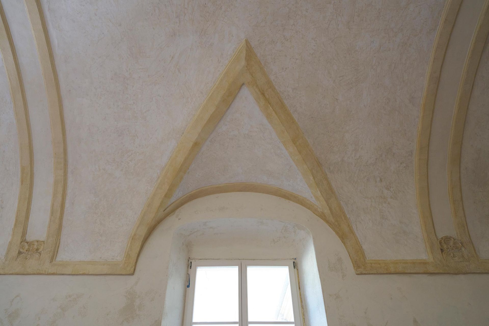 Soffitto a volta a crociera con costoloni e pareti chiare, sopra una finestra ad arco.