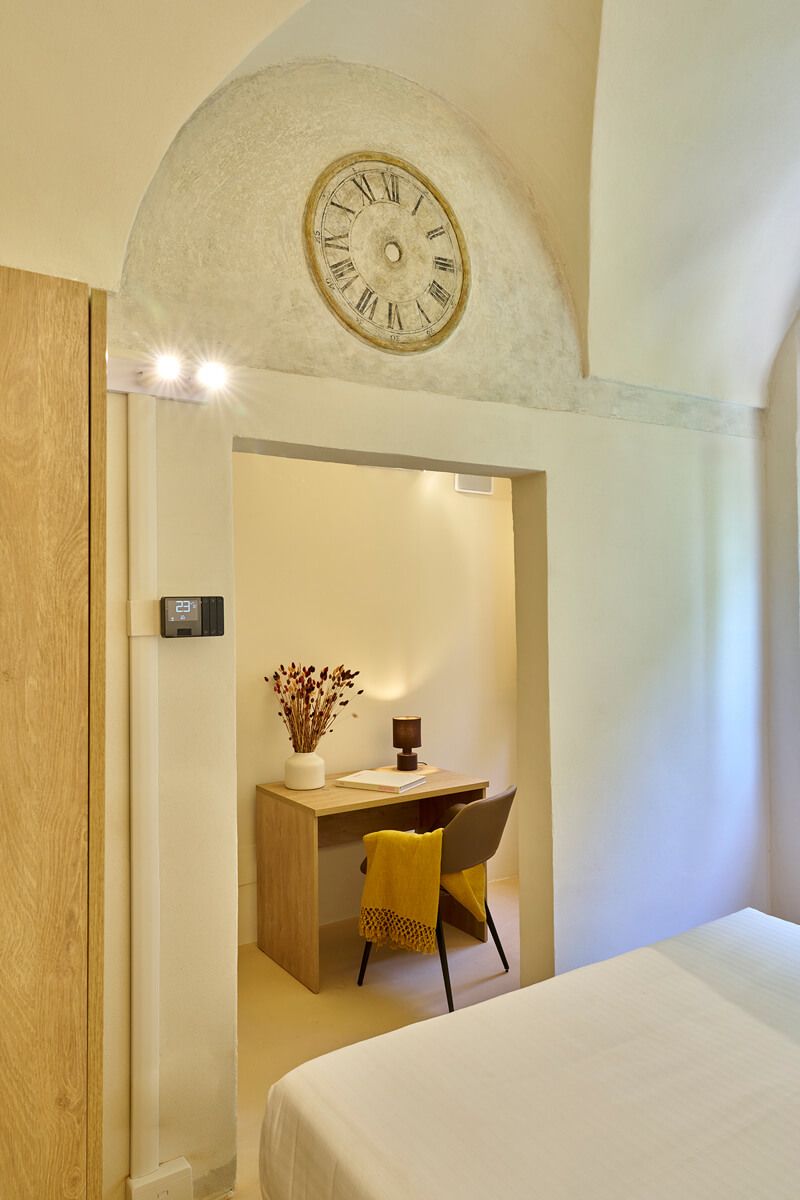 Camera con soffitto a volta e grande orologio a parete, con scrivania in legno sistemata in una nicchia.